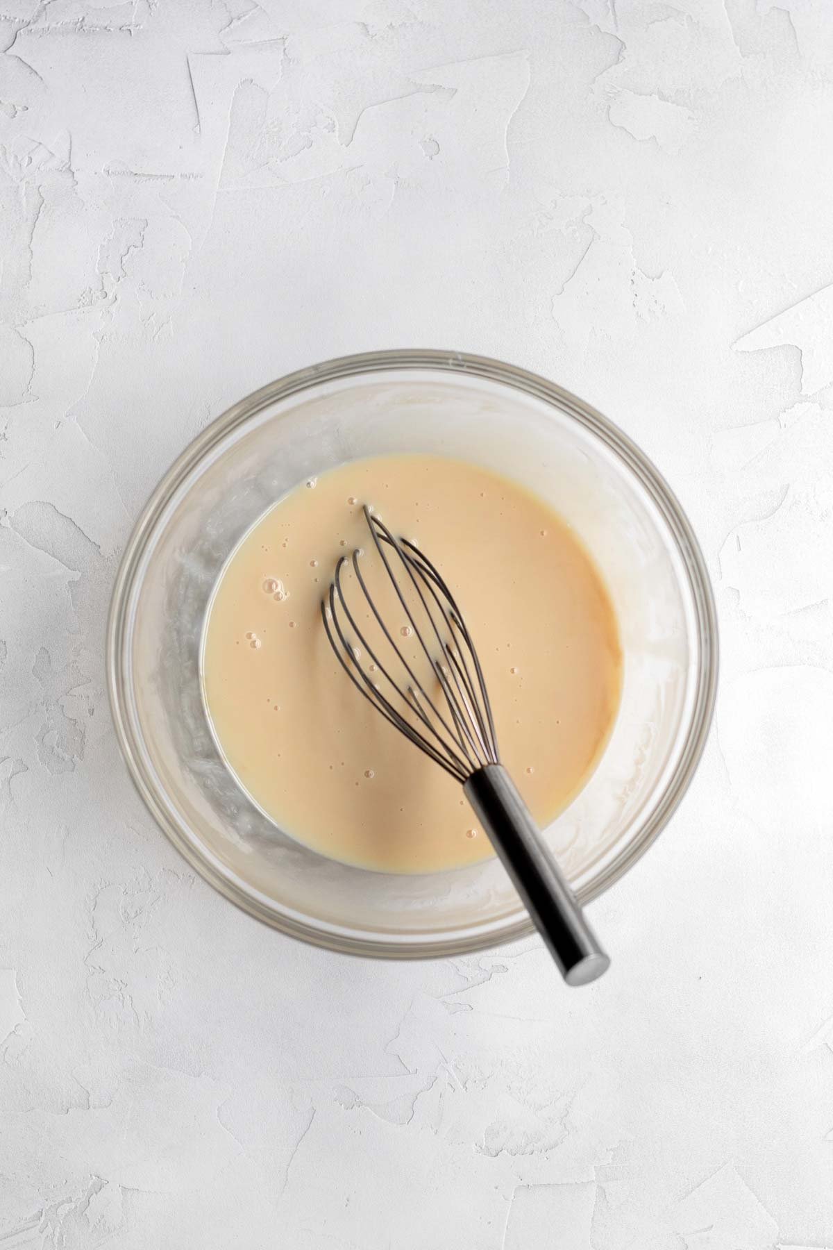 Salt, vanilla and condensed milk mixed in a bowl with a whisk.