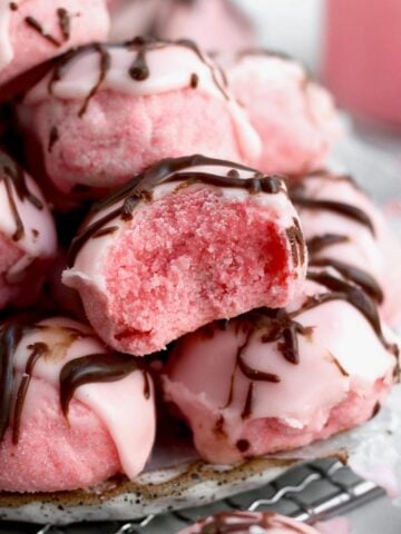 Pile of Strawberry Shortbread Cookies with one missing a bite exposing its lite and sugary interior.