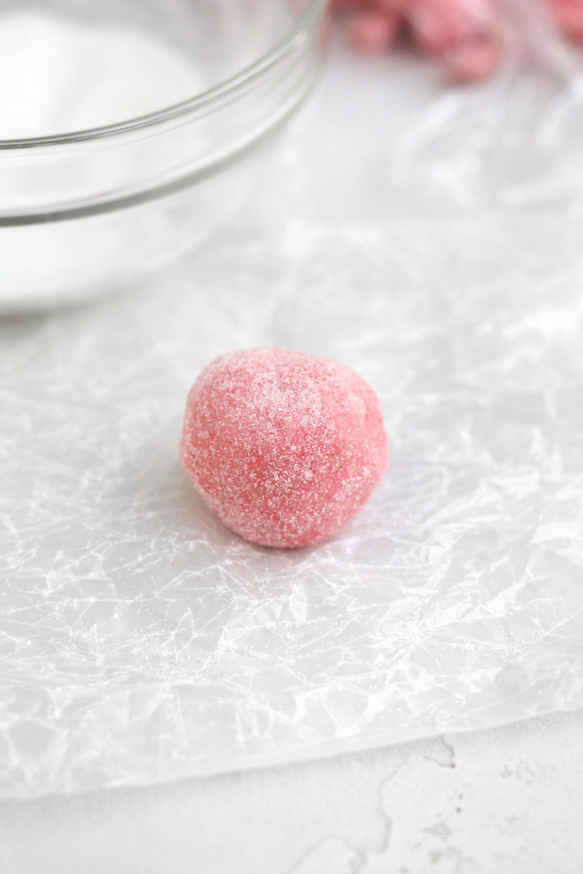 A scooped ball of Strawberry Shortbread cookie dough covered in sugar.