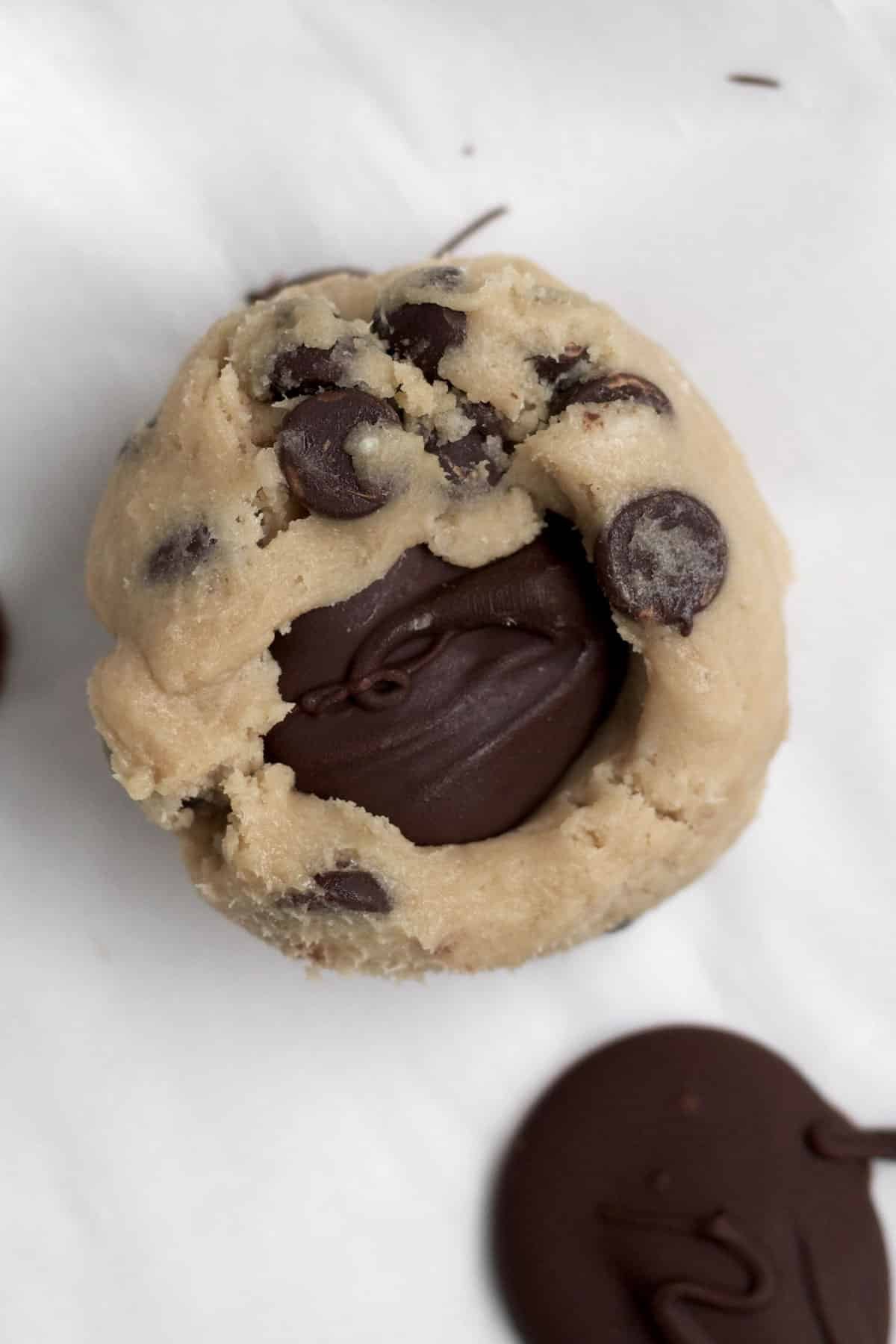 Pressing the chocolate dollops into a scooped ball of cookie dough.