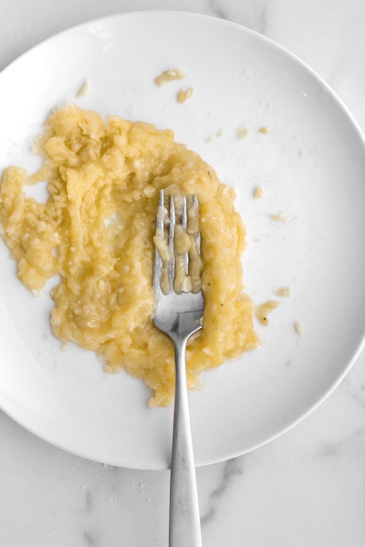 Mashing bananas on a plate with a fork.