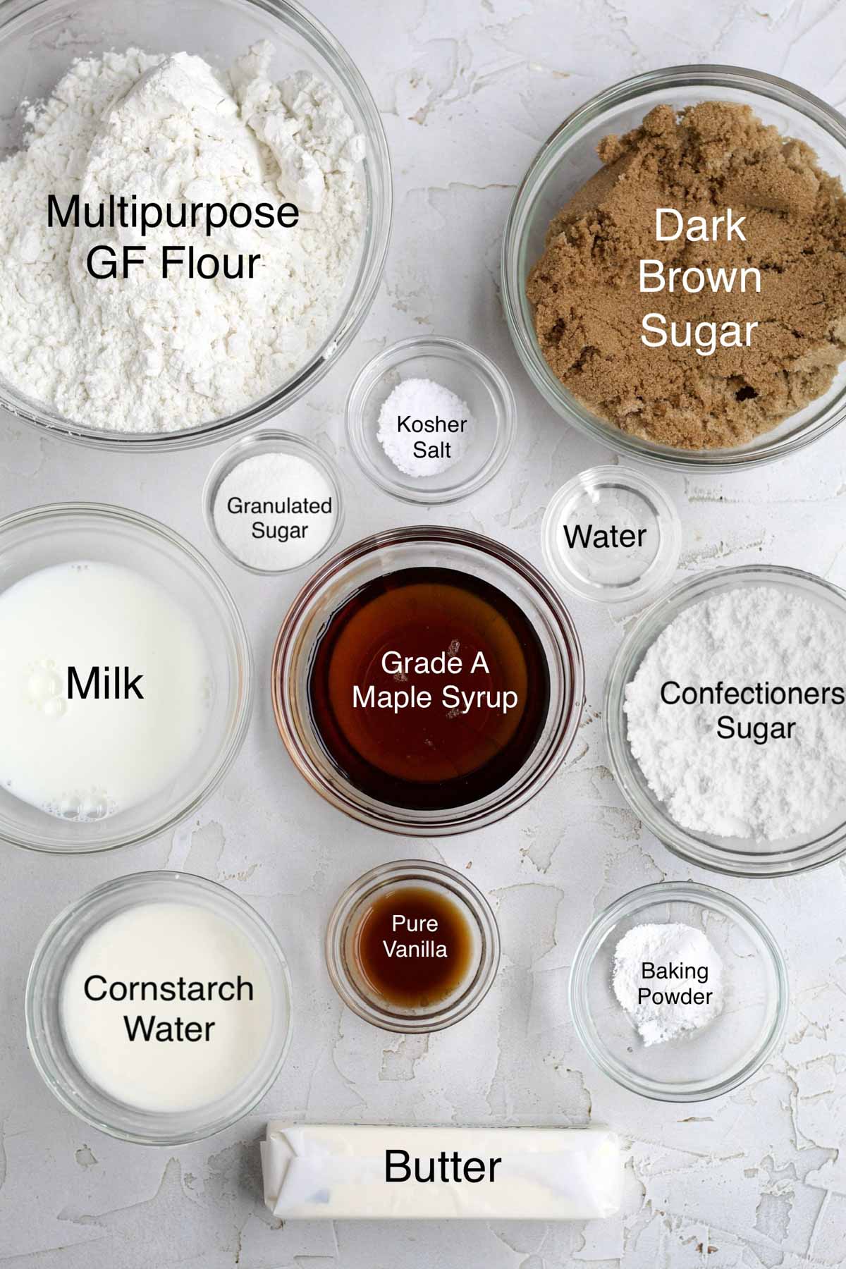 Bowls of Multipurpose Gluten Free Flour, dark brown sugar, milk, granulated sugar, kosher salt, water, Grade A maple syrup, confectioners' sugar, cornstarch water, pure vanilla, baking powder and butter.