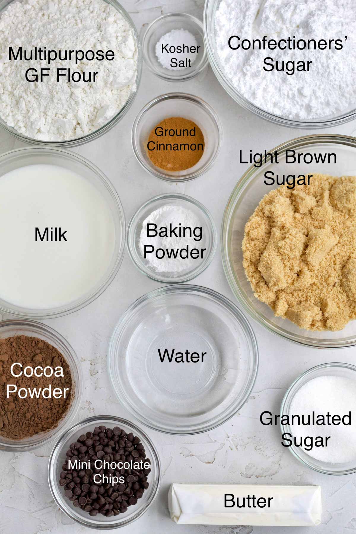 Bowls of multipurpose gluten free flour, kosher salt, confectioners' sugar, ground cinnamon, light brown sugar, milk, baking powder, cocoa powder, water, granulated sugar, mini chocolate chips, and butter.