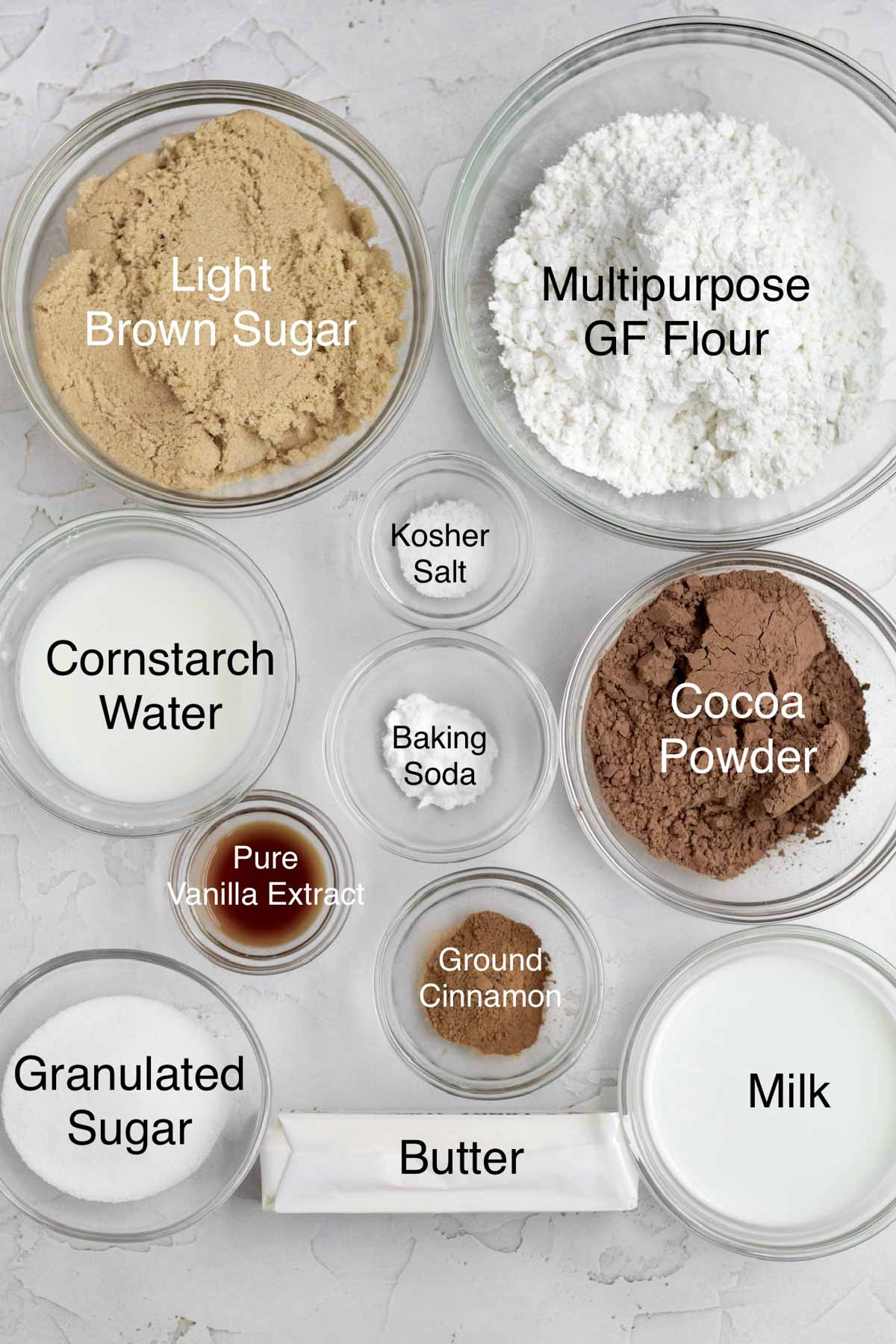Bowls of light brown sugar, multipurpose gluten free flour, cornstarch water, kosher salt, baking soda, cocoa powder, pure vanilla extract, ground cinnamon, granulated sugar, butter and milk.