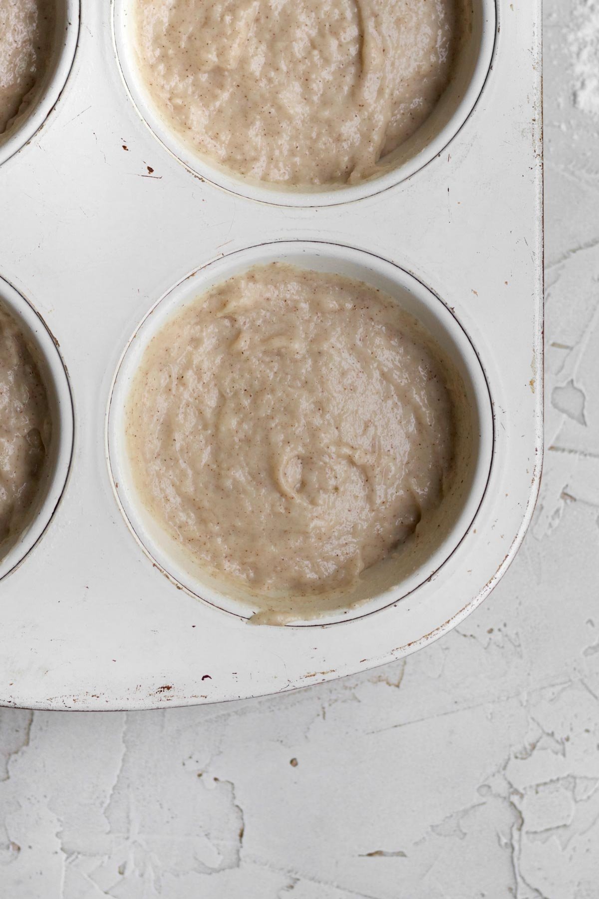Filling a muffin tin with the applesauce muffin batter and smoothing out the tops.