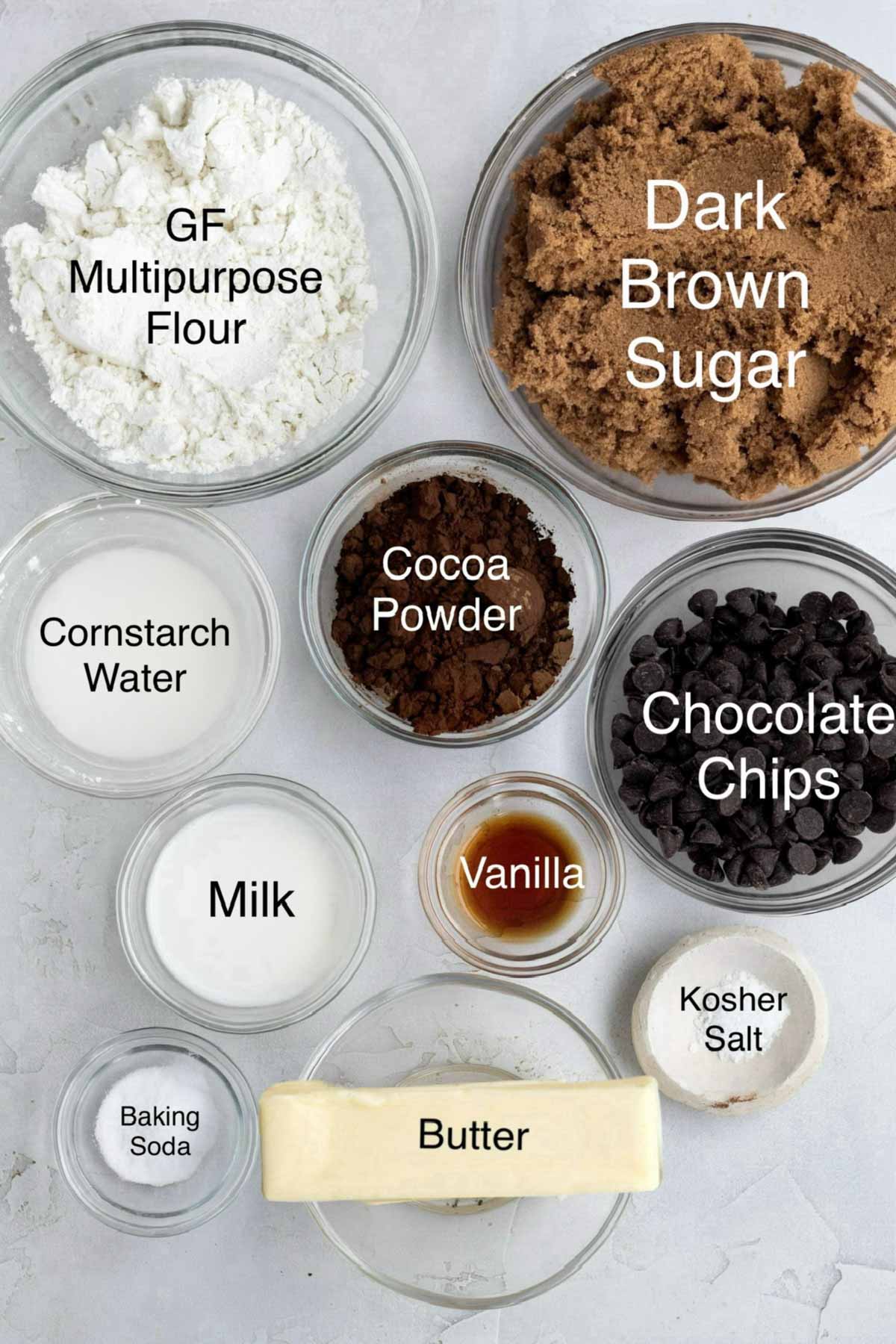 Gluten free Flour, dark brown sugar, cornstarch water, cocoa powder, chocolate chips, milk, vanilla, salt, baking soda, and butter in separate bowls.