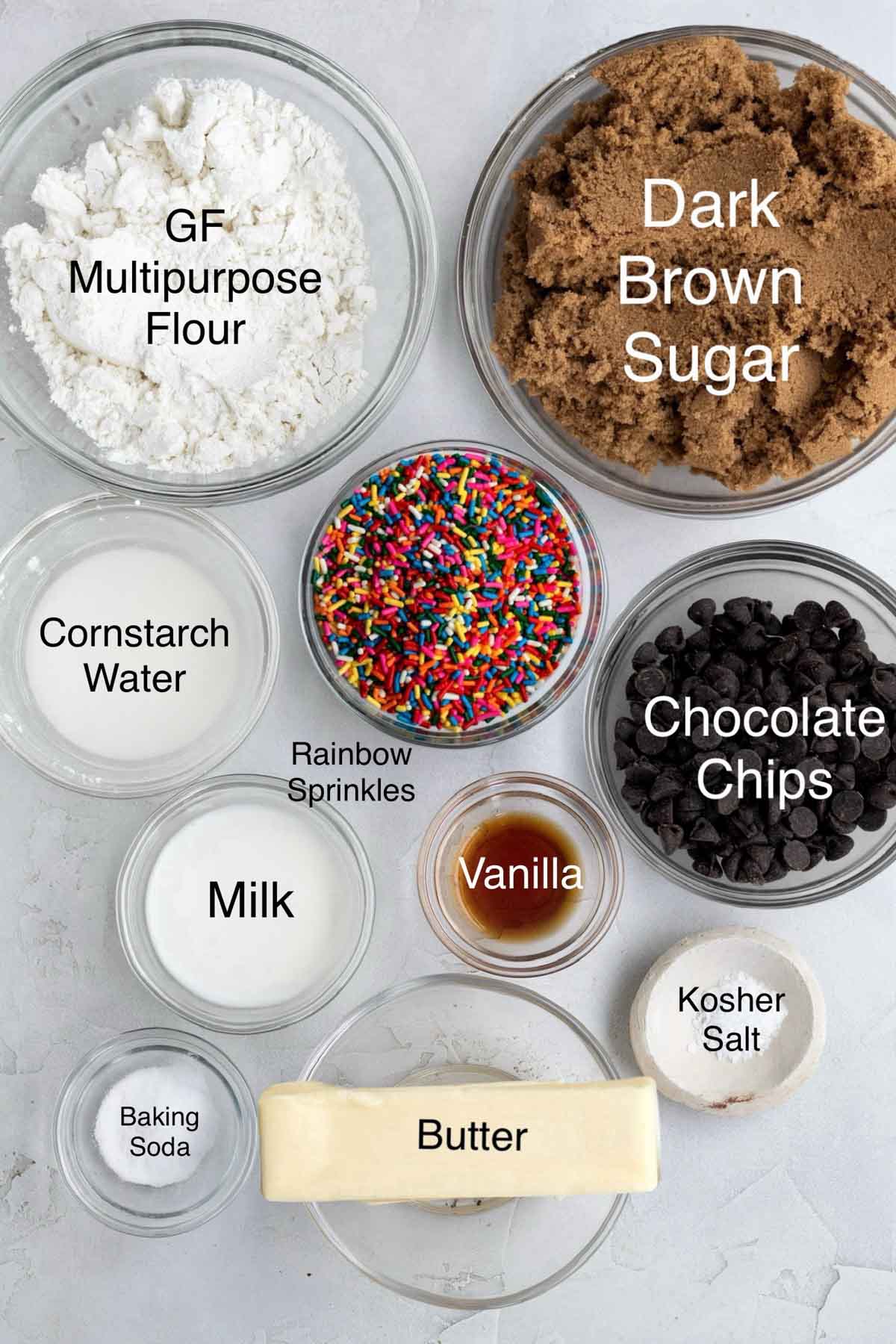 Bowls of gluten free multipurpose flour, dark brown sugar, cornstarch water, rainbow sprinkles, chocolate chips, milk, vanilla, kosher salt, baking soda, and butter.