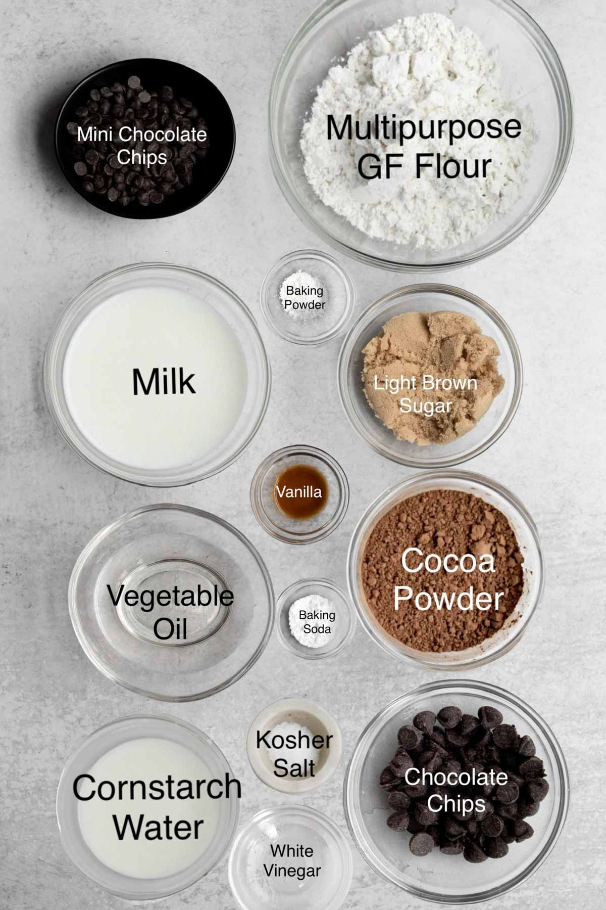 Bowls of mini chocolate chips, multipurpose gluten free flour, milk, baking powder, light brown sugar, vanilla, vegetable oil, baking soda, cocoa powder, cornstarch water, kosher salt, chocolate chips, and white vinegar.