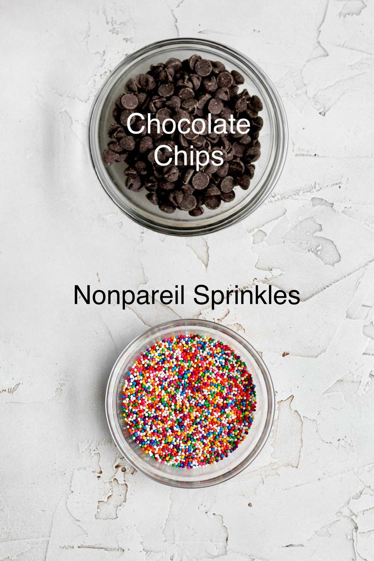 Separate bowls of chocolate chips and rainbow nonpareil sprinkles.
