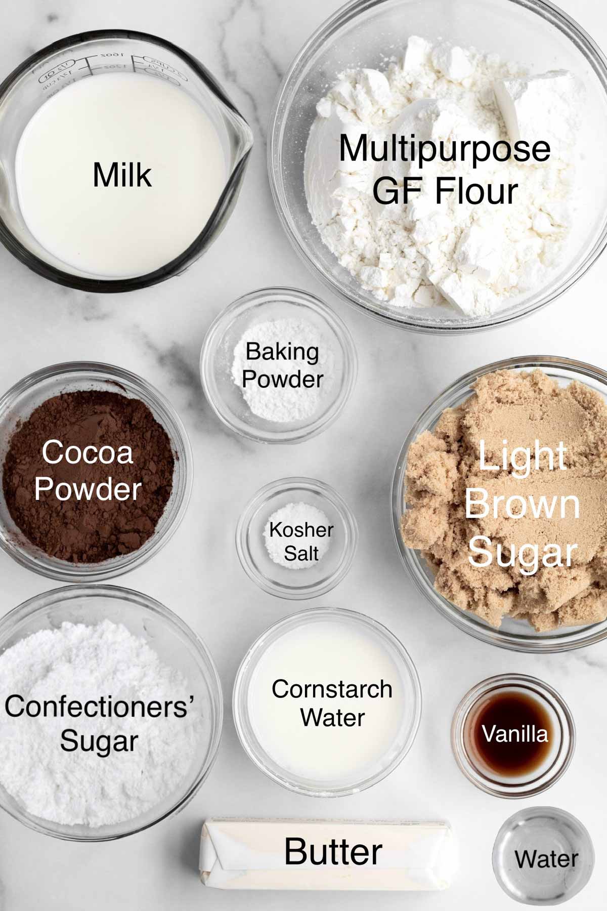 Separate containers of milk, gluten free flour, cocoa powder, baking powder, light brown sugar, kosher salt, confectioners' sugar, cornstarch water, vanilla, butter, and water.