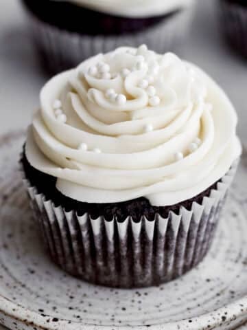 A chocolate cupcake with vanilla frosting adorned with white nonpareils.