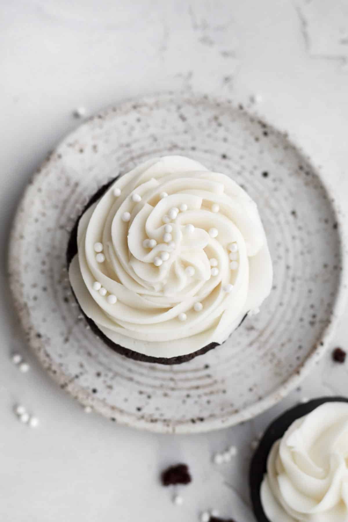 Piping a swirl of vanilla frosting atop the chocolate cupcake and adding white sprinkles.