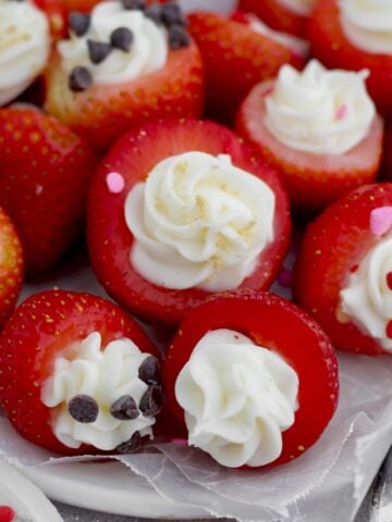 Juicy Cheesecake Stuffed Strawberries topped with chocolate chips, heart sprinkles and graham cracker.