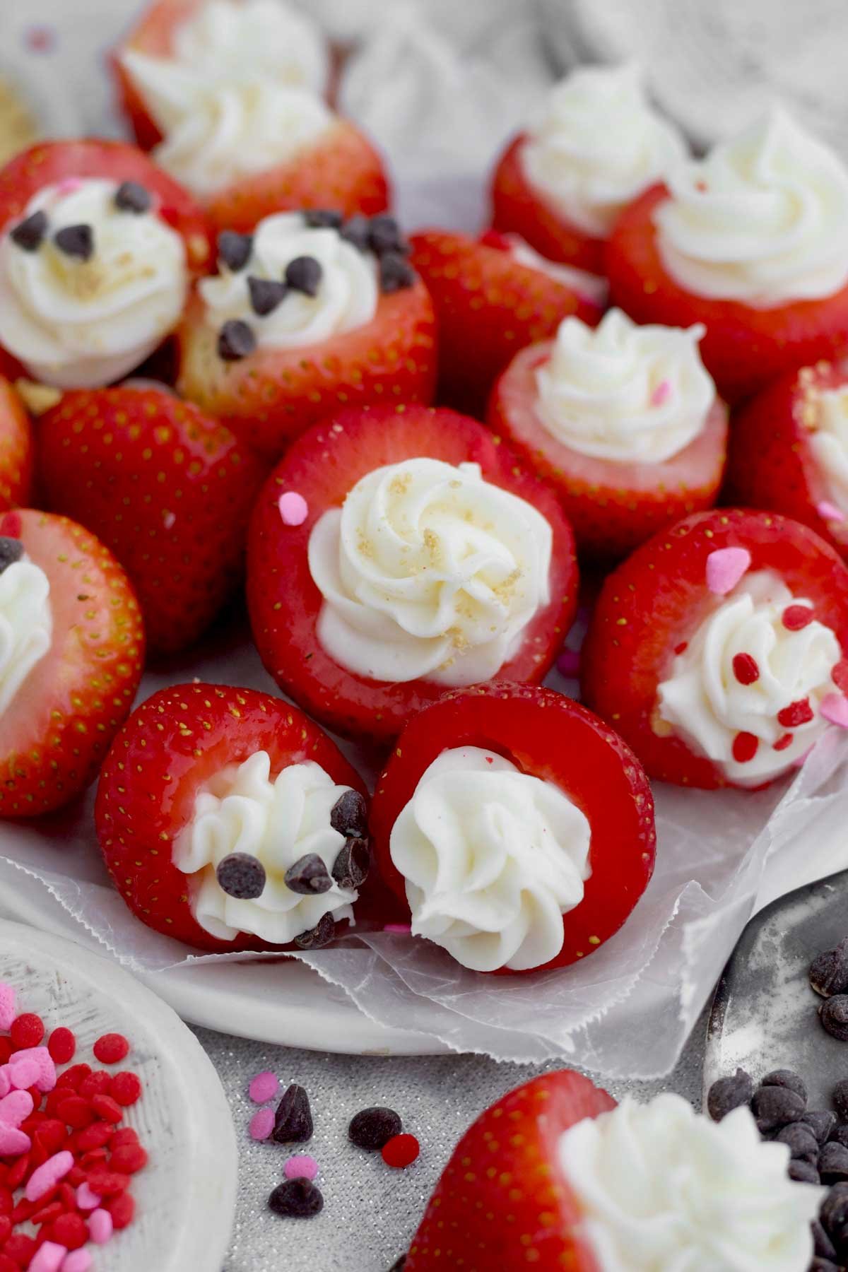 Juicy Cheesecake Stuffed Strawberries topped with chocolate chips, heart sprinkles and graham cracker.