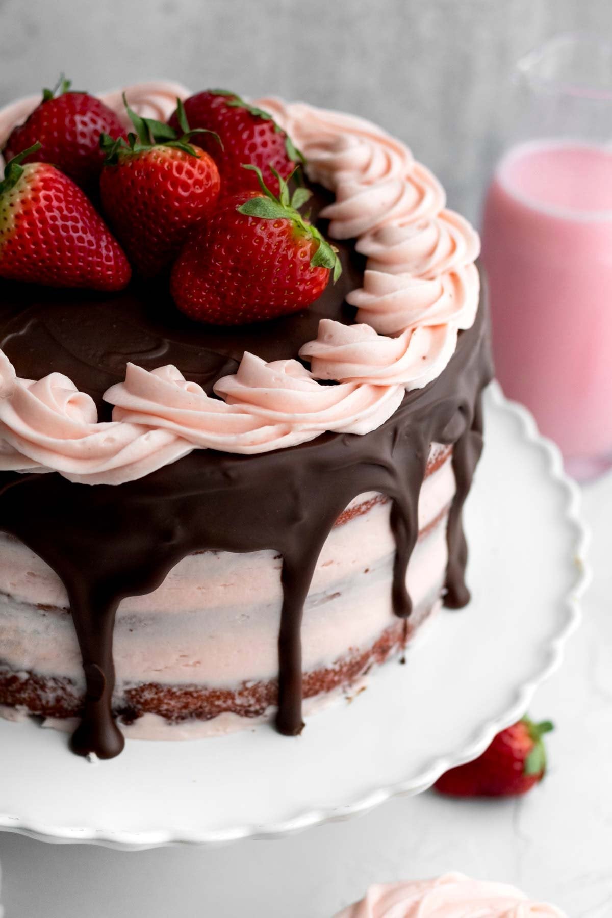 Loops of sweet strawberry buttercream piped on a strawberry frosted cake with whole strawberries and chocolate.