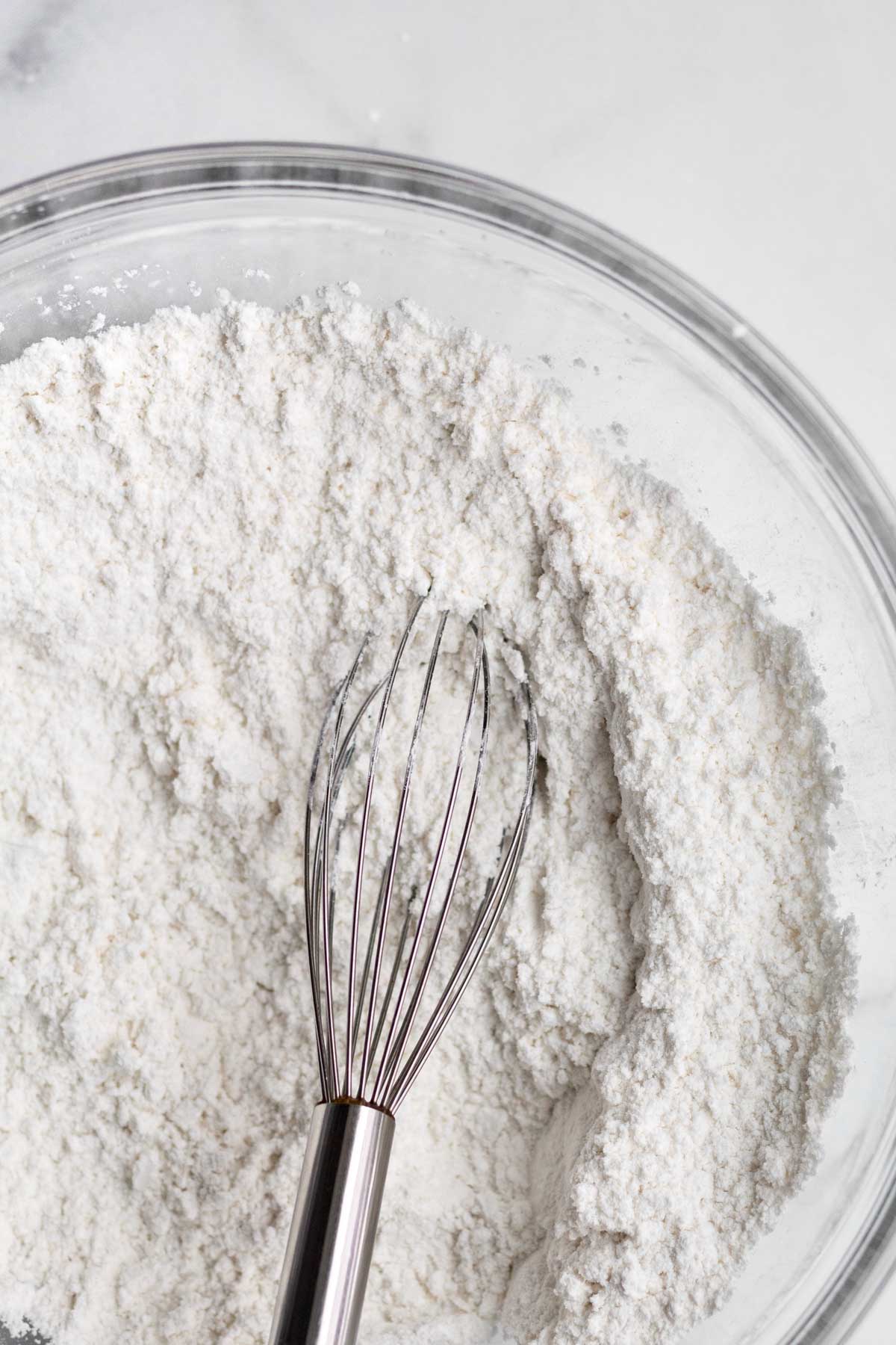 A whisk with the white gluten free dry ingredients.