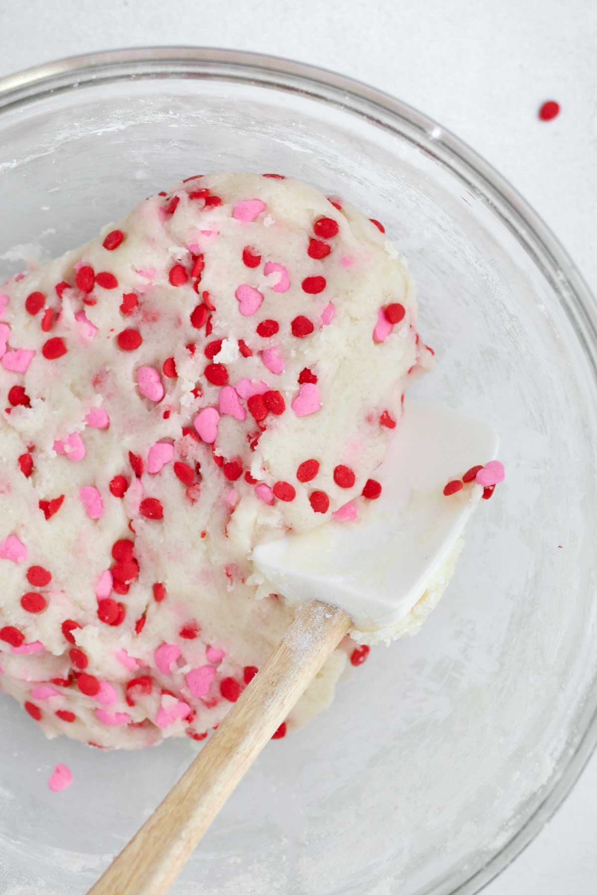 The cookie dough being mixed with pink and red heart-shaped sprinkles.