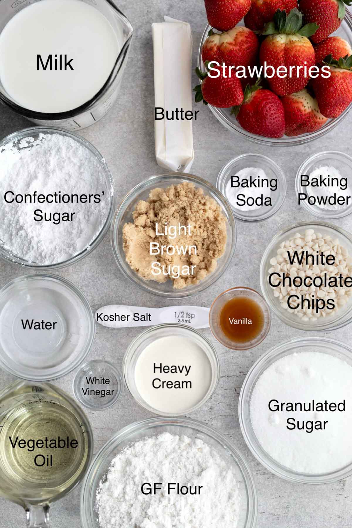 Separate containers of milk, butter, strawberries, confectioners' sugar, light brown sugar, baking soda, baking powder, water, kosher salt, vanilla, white chocolate chips, white vinegar, heavy cream, granulated sugar, vegetable oil, and gluten free flour.