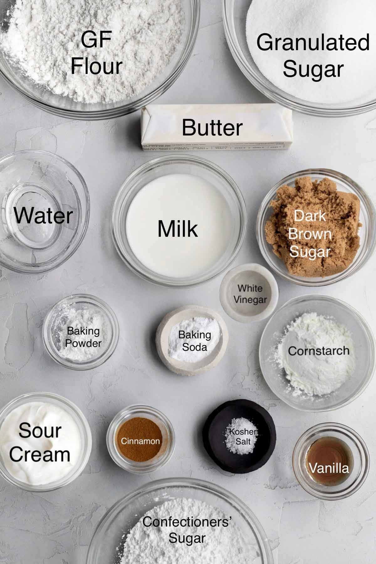 coffee cake muffin ingredients in separate containers: gluten free flour, granulated sugar, butter, water, milk, dark brown sugar, baking powder, white vinegar, cornstarch, sour cream, cinnamon, kosher salt, vanilla, and confectioners' sugar.