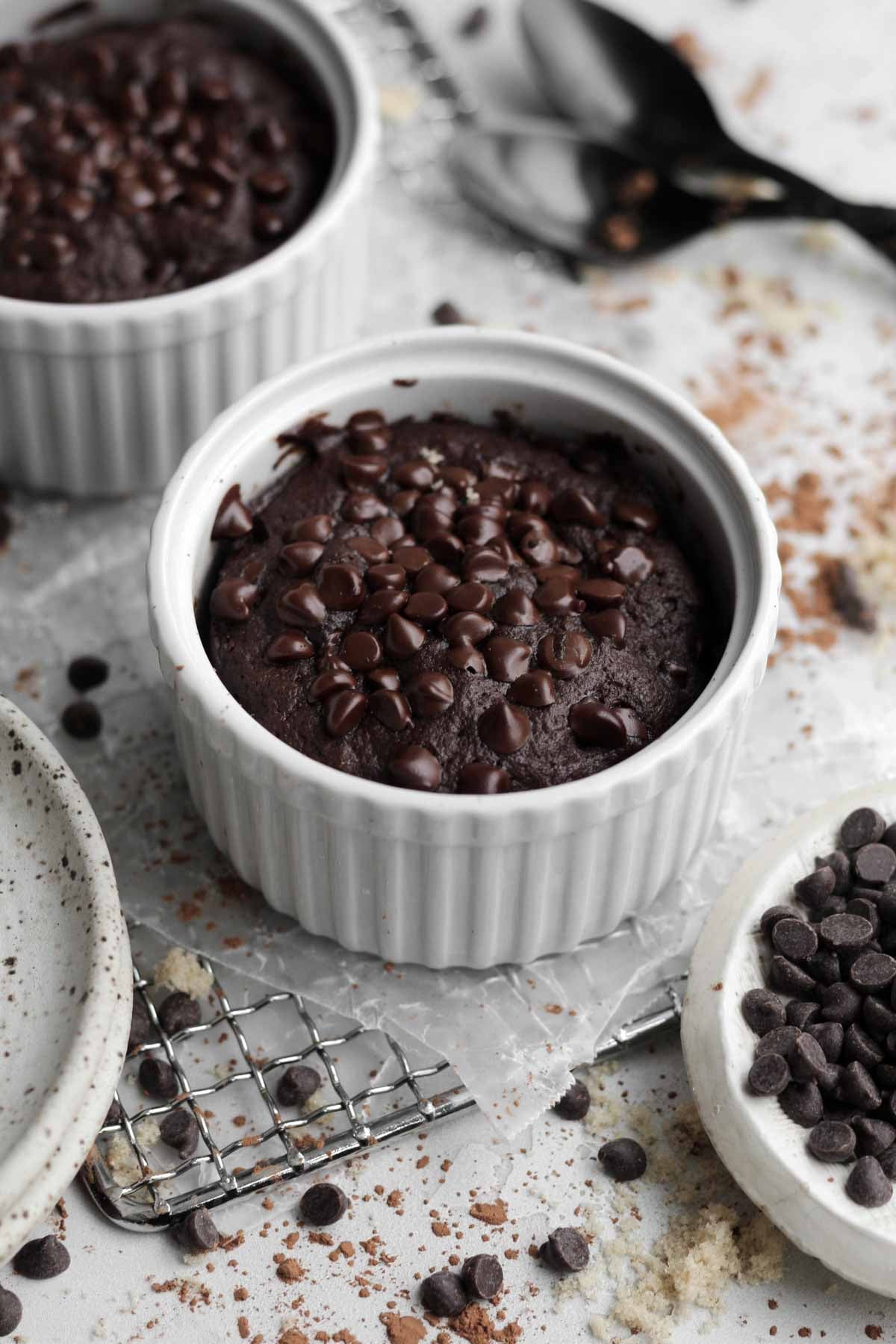 Warm, egg-free, easy chocolate mug cakes in fluted white ramekins with sweet chocolate chips.