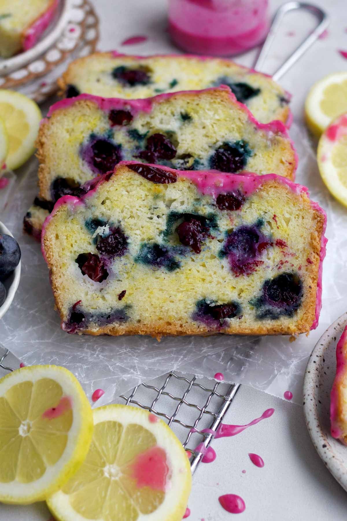 Three slices of gluten-free Lemon Blueberry loaf with bursted baked blueberries and sweet magenta glaze.