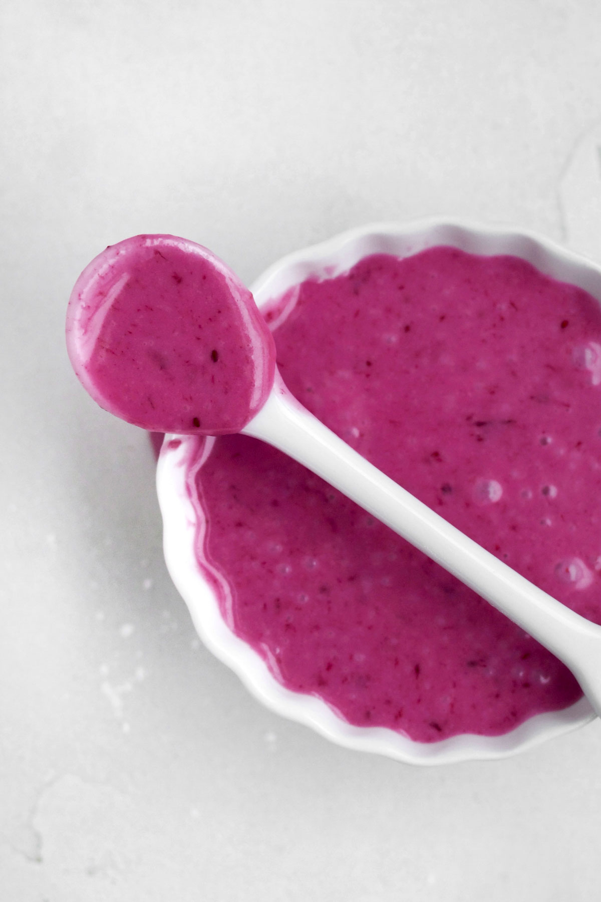 Bright magenta sugary blueberry glaze in a ramekin with a spoon.