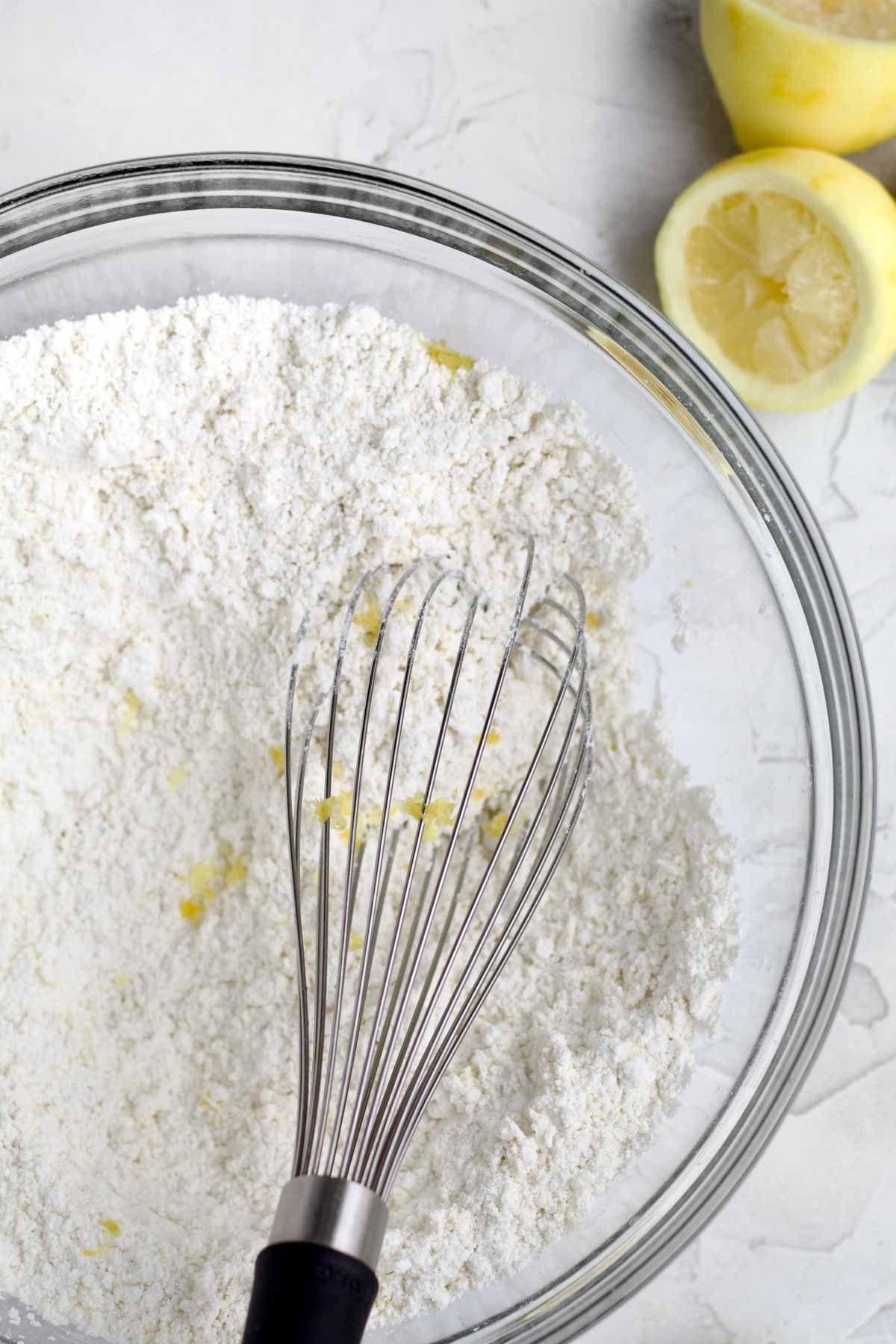 A whisk with the white dry ingredients and some lemon zest.