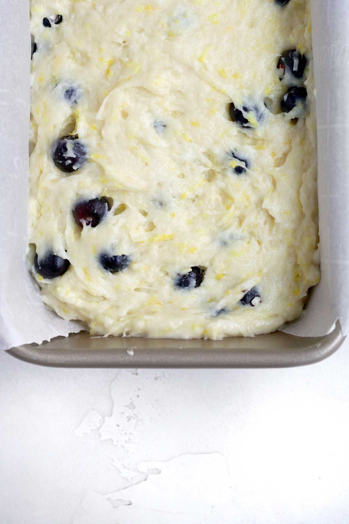 Filling a loaf pan with the blueberry lemon loaf batter.