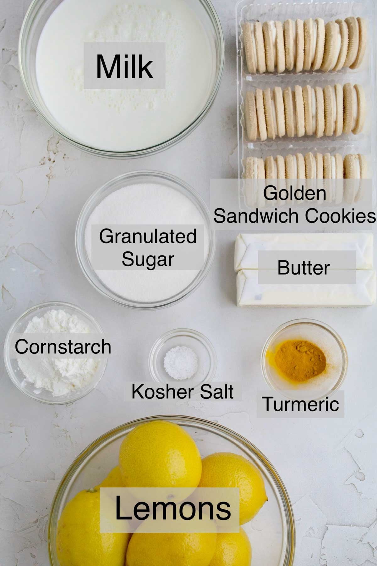 lemon curd pie ingredients in separate containers: milk, golden sandwich cookies, granulated sugar, butter, cornstarch, kosher salt, turmeric, and lemons.