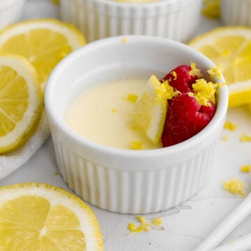 creamy eggless lemon posset dessert with fresh red raspberries, lemon wedge, and lemon zest.