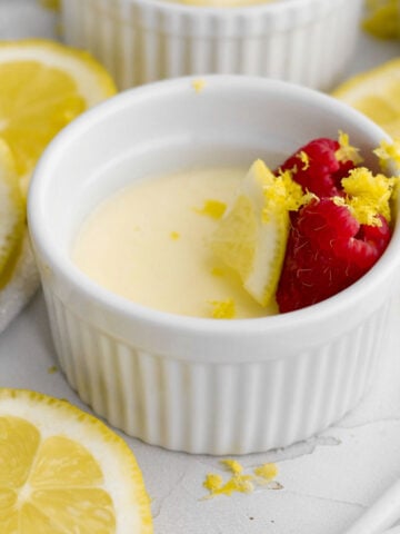 creamy eggless lemon posset dessert with fresh red raspberries, lemon wedge, and lemon zest.