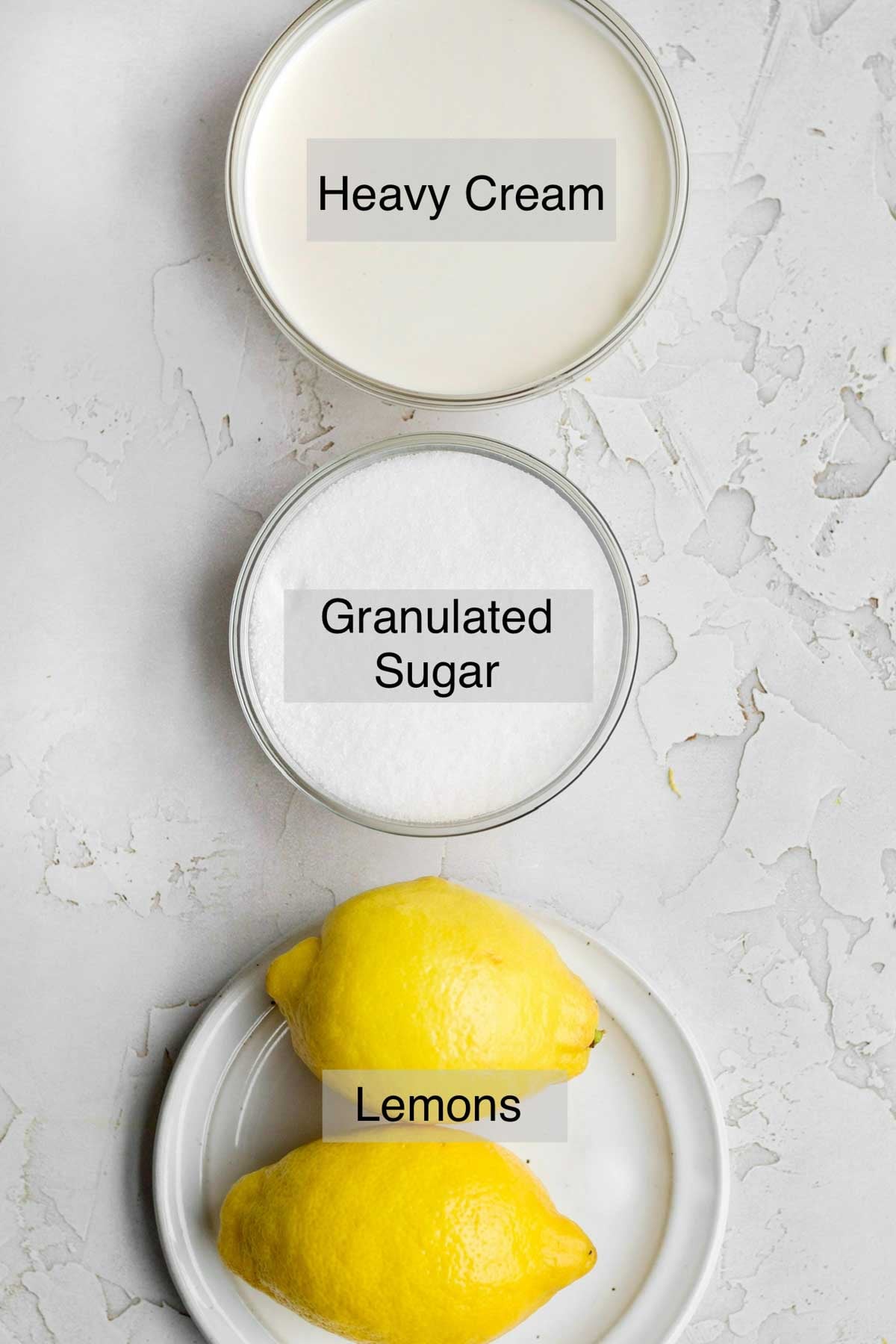 lemon posset ingredients in separate containers: heavy cream, granulated sugar, and lemons.