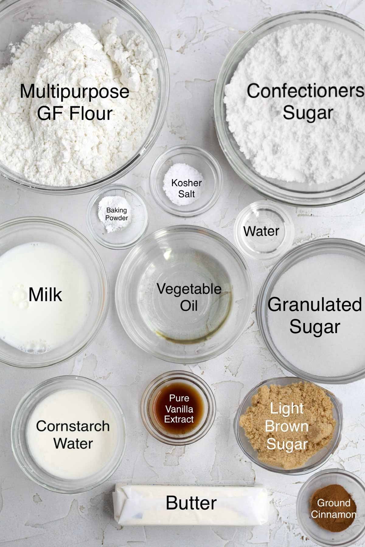 new york crumb cake ingredients in separate containers: multipurpose gluten free flour, confectioners' sugar, milk, baking powder, kosher salt, water, vegetable oil, granulated sugar, cornstarch water, pure vanilla extract, light brown sugar, butter, and ground cinnamon.