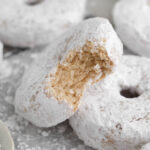 A bitten gluten free powdered sugar donut revealing its soft baked crumb interior.