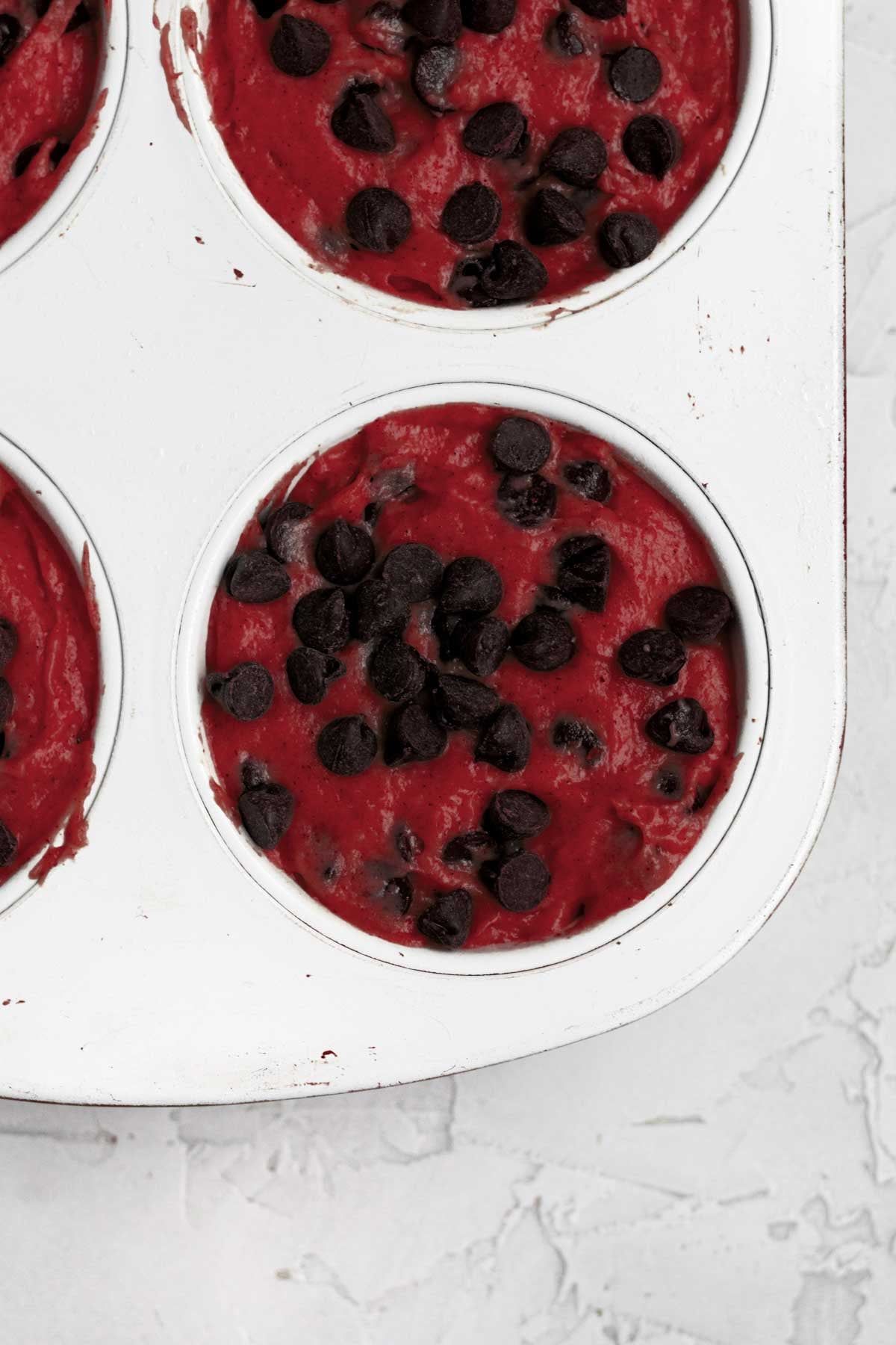 filling a muffin tin with red velvet muffin batter and adding extra chocolate chips.