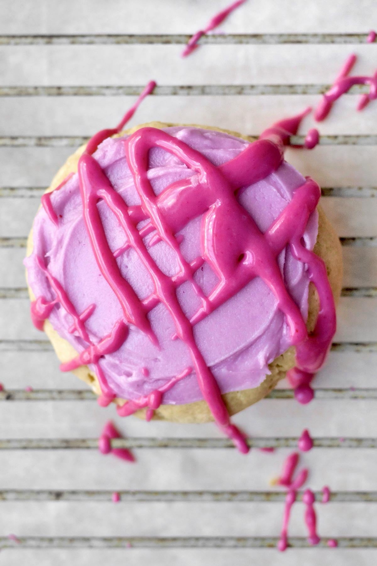 icing the frosted brown sugar cookies with the magenta blueberry icing in a cross-hatch pattern.