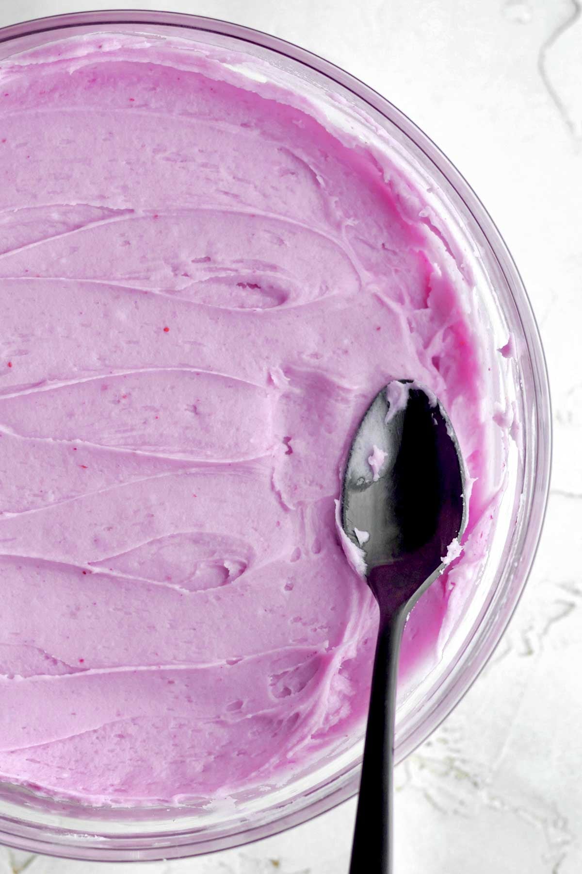 creamy, lilac-colored blueberry cream cheese frosting smoothed out in a bowl with a spoon.
