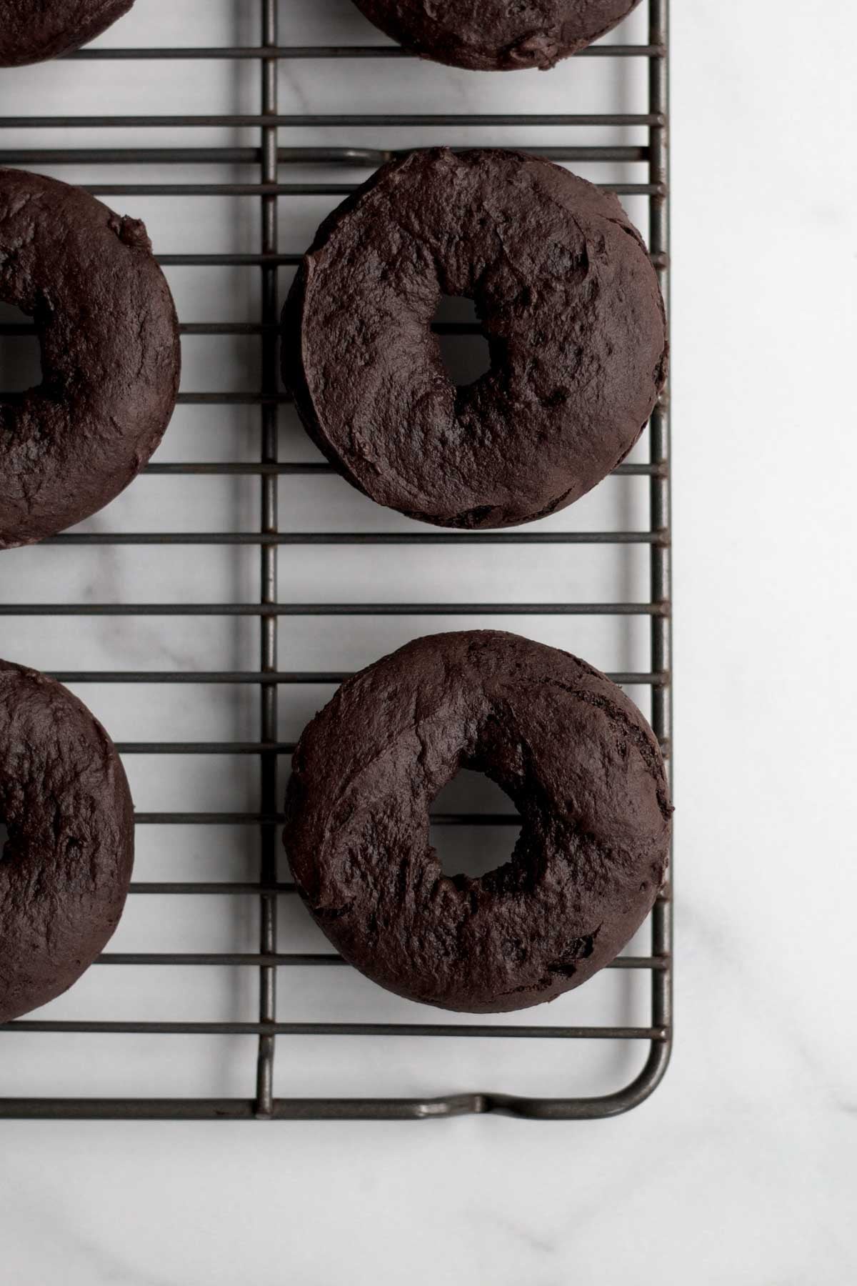 fresh-baked chocolate donut bases resting on a wire rack.