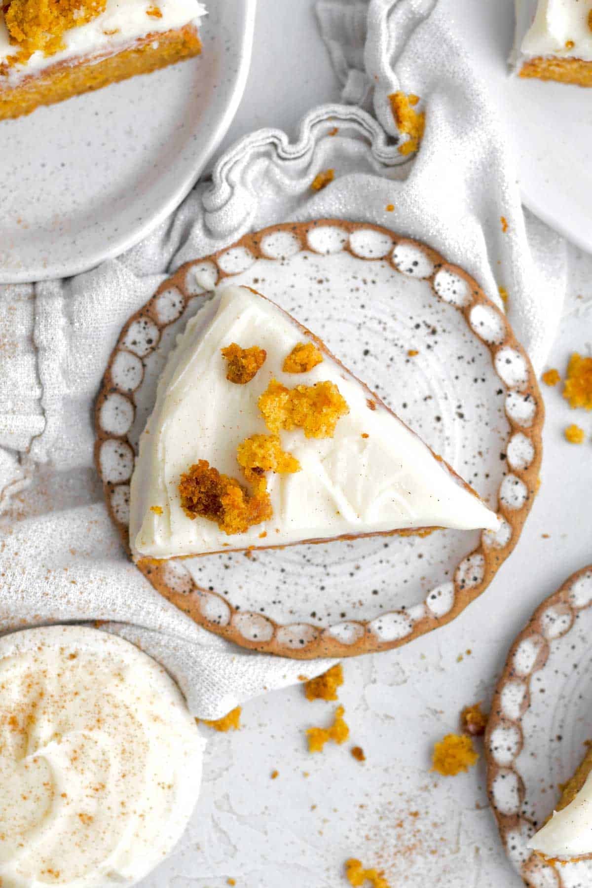 a triangular slice of easy eggless carrot cake with creamy frosting on a speckled plate.