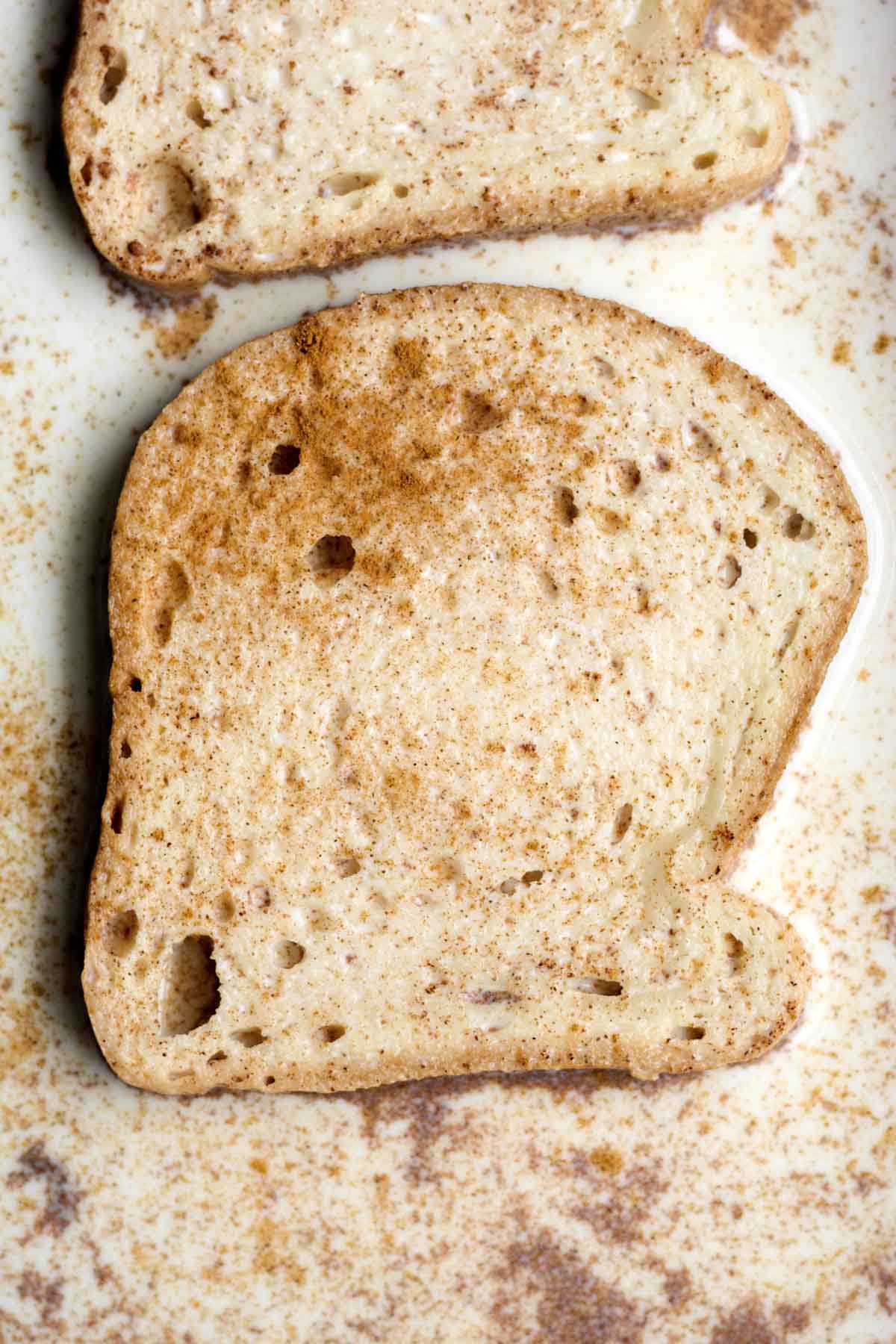 sliced gluten-free bread soaking in a pan of cinnamon milk.
