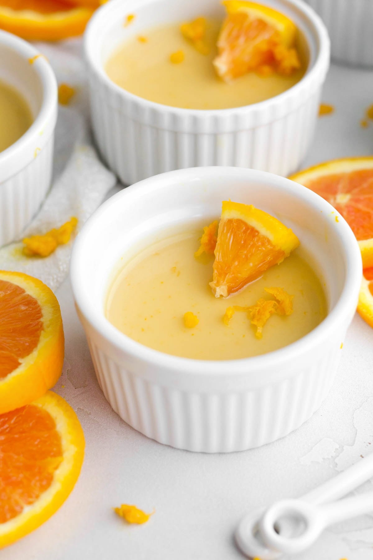 luscious orange posset in a ruffled ramekin garnished with citrus zest and an orange slice.
