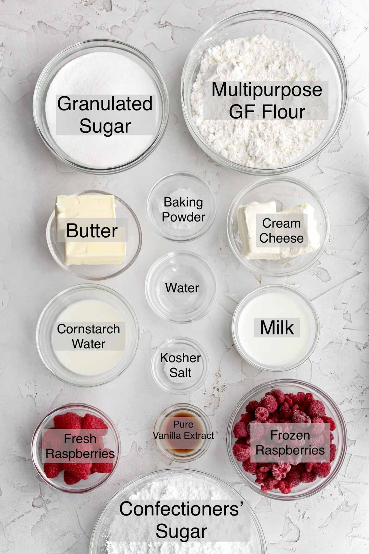 raspberry cheesecake cookies ingredients in separate containers: granulated sugar, multipurpose gluten free flour, butter, baking powder, cream cheese, water, cornstarch water, kosher salt, milk, fresh raspberries, pure vanilla extract, frozen raspberries, and confectioners' sugar.