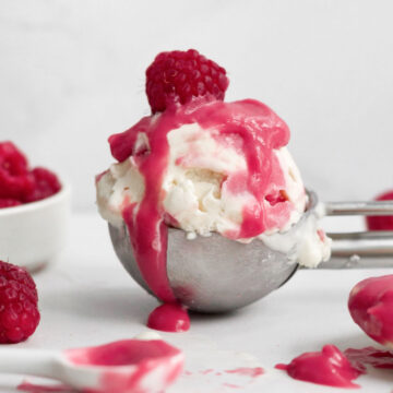 tempting scoop of raspberry ripple ice cream drizzled with extra raspberry curd and a fresh raspberry.
