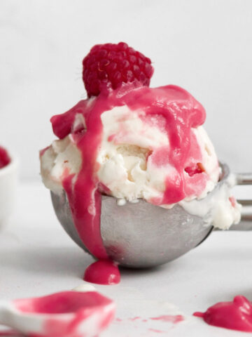 tempting scoop of raspberry ripple ice cream drizzled with extra raspberry curd and a fresh raspberry.