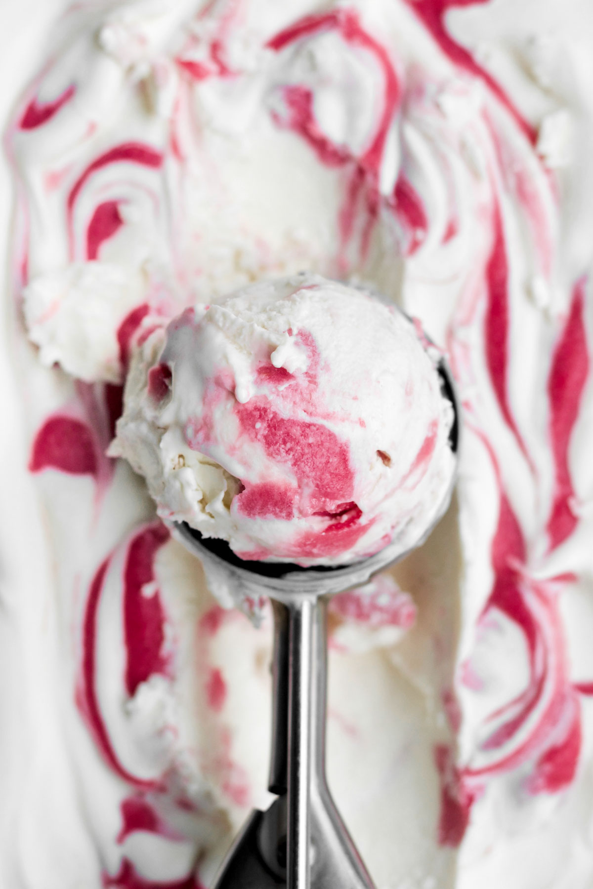 a scoop of raspberry ripple ice cream with a beautiful swirl of frozen vibrant raspberry curd.
