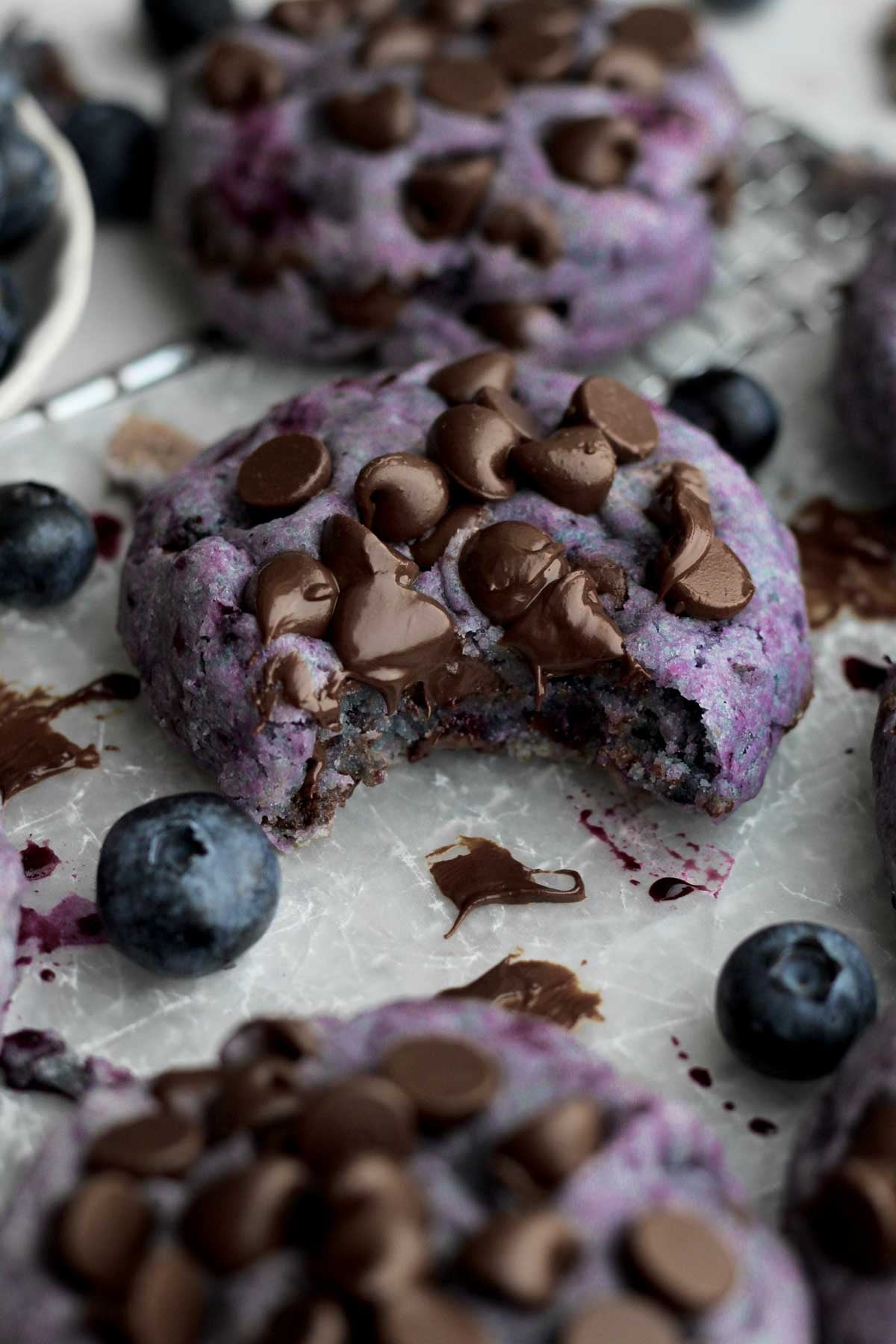 Glistening pools of melted chocolate descend into the soft interior of the bitten chocolate chip blueberry cookie.