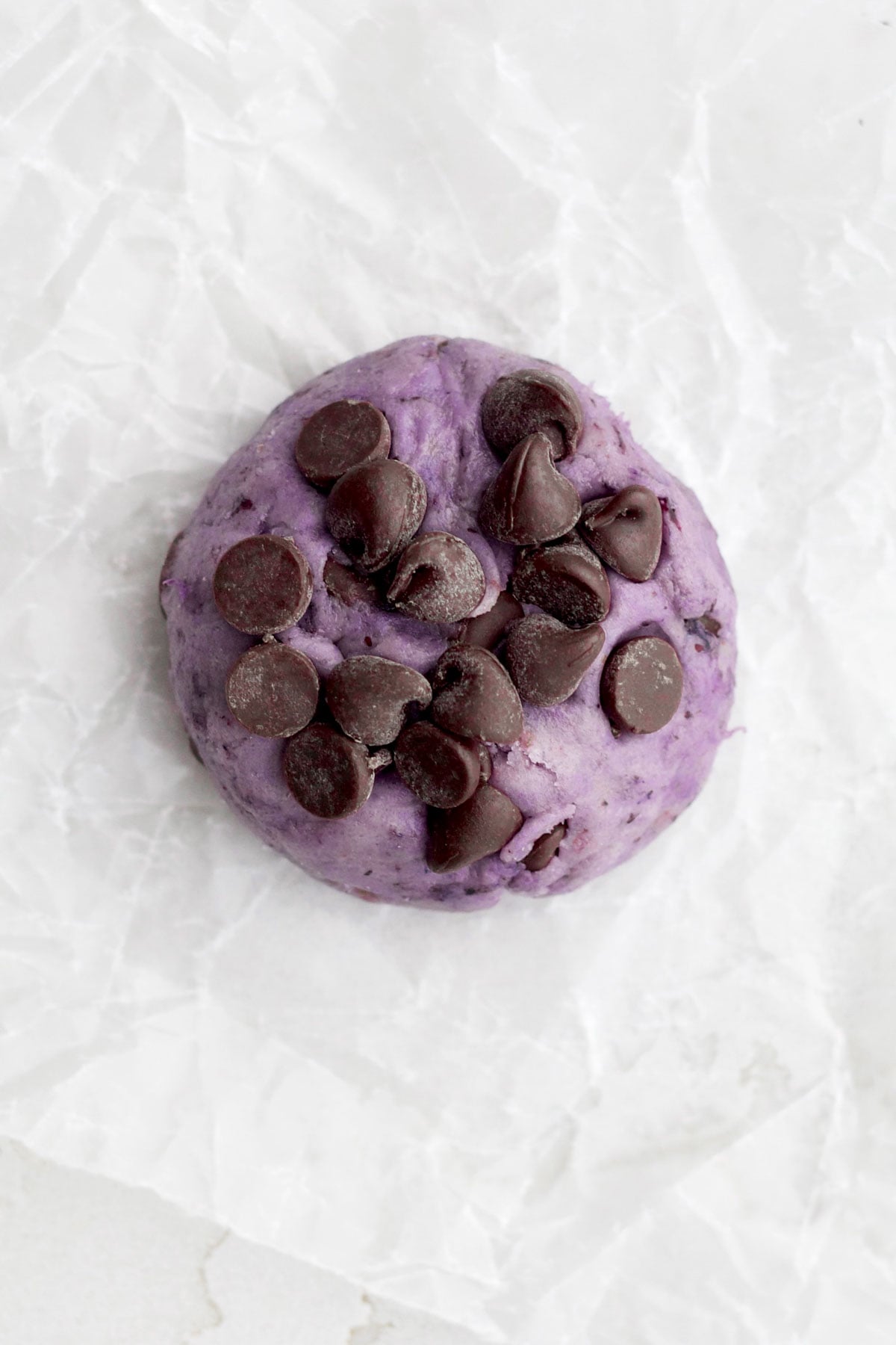 Adding chocolate chips to the top of the purple blueberry cookie.
