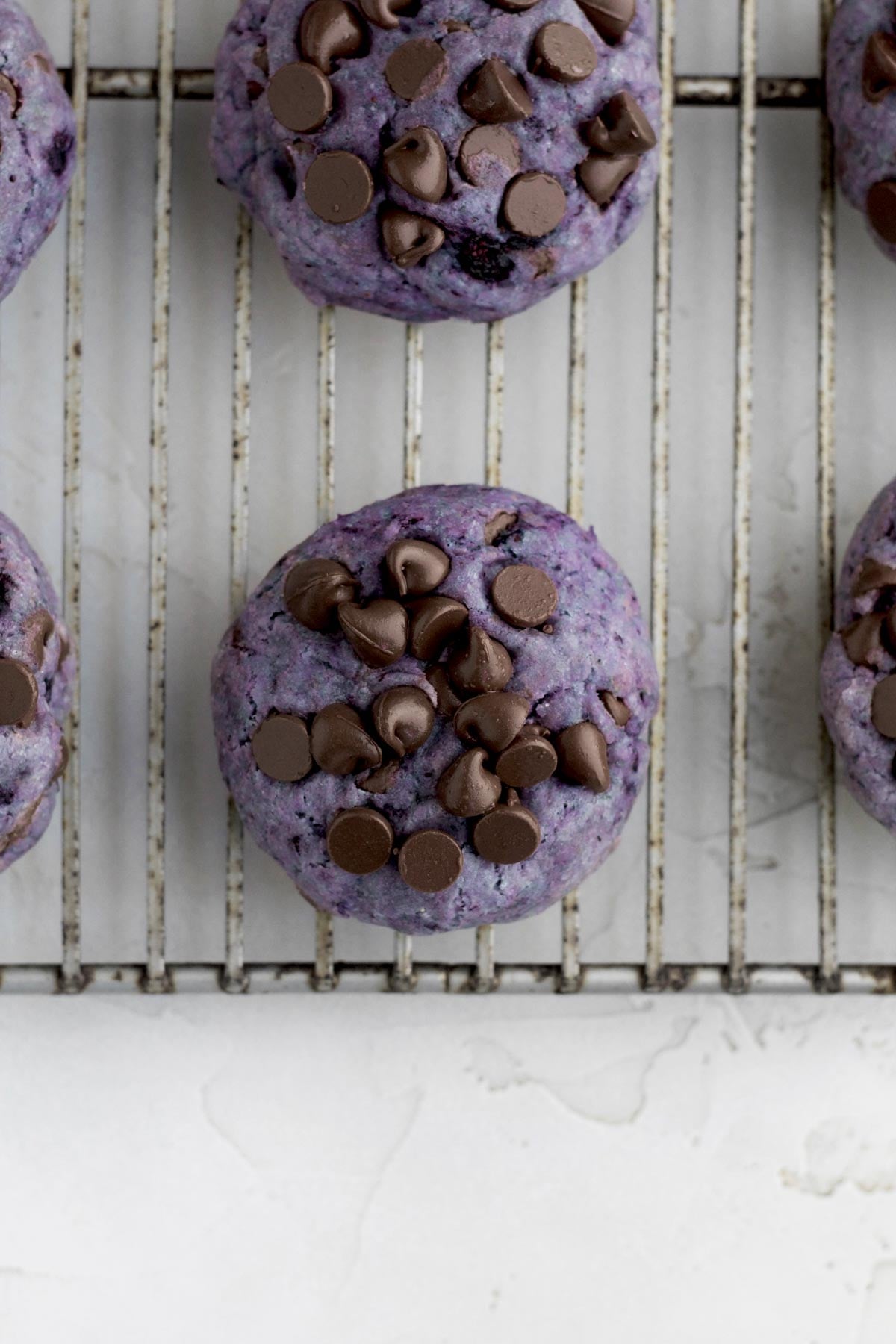 Fresh-baked chocolate chip blueberry cookies with slightly melted chocolate chips resting on a wire rack.