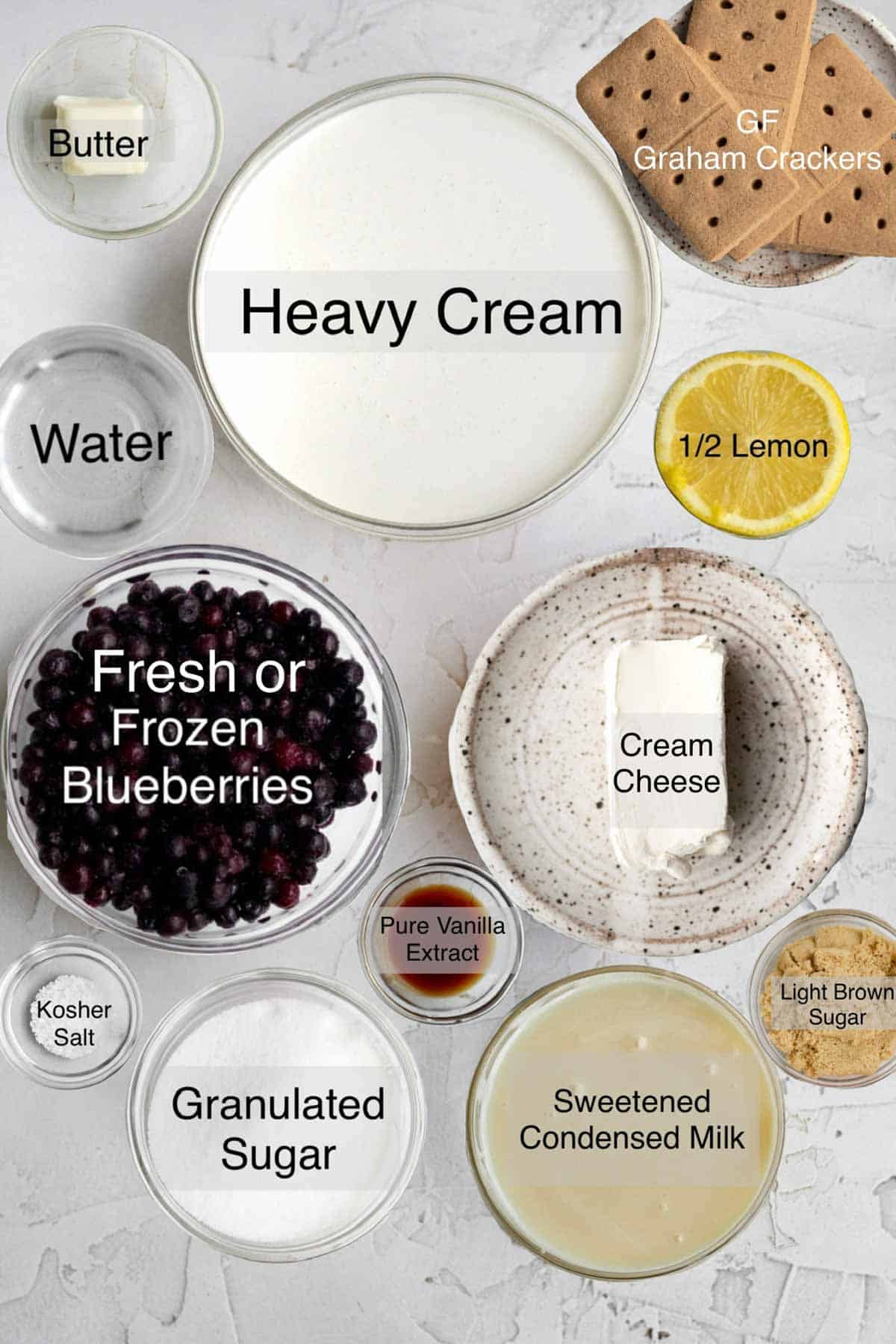 blueberry cheesecake ice cream ingredients in separate bowls: butter, heavy cream, gluten free graham crackers, water, a halved lemon, blueberries, cream cheese, kosher salt, granulated sugar, pure vanilla extract, sweetened condensed milk, light brown sugar.
