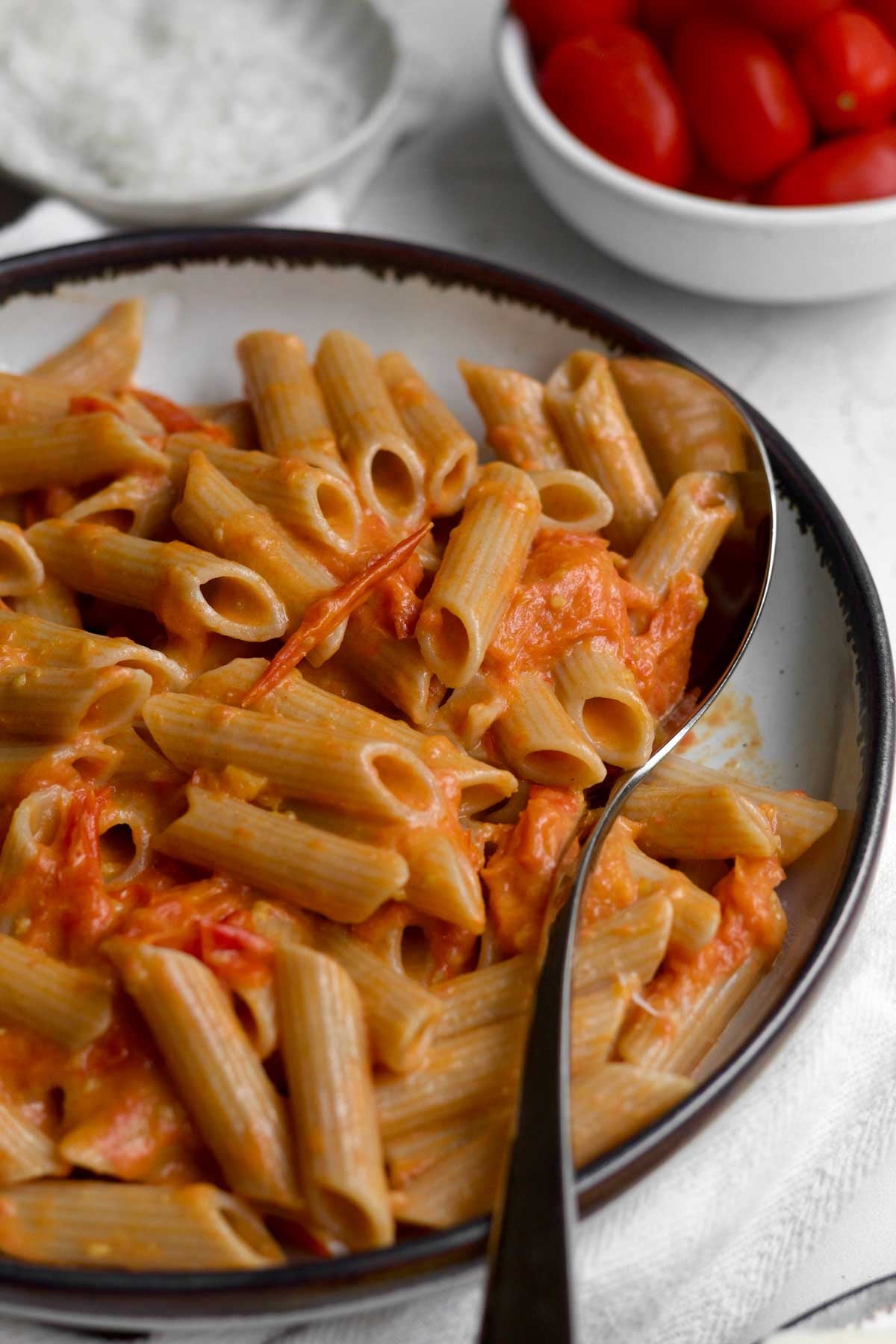 A silver serving spoon scoops the cherry tomato pasta from a bowl.